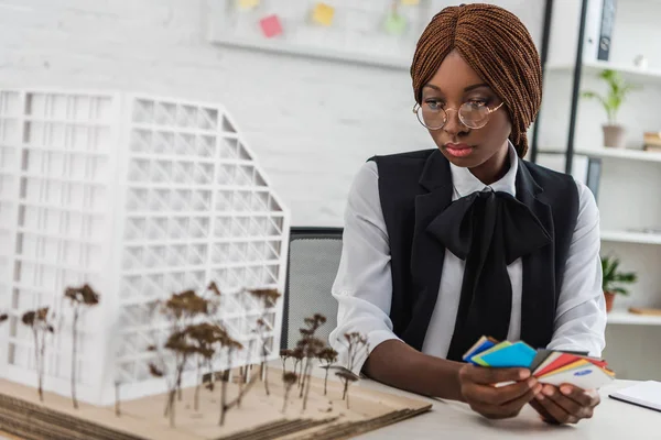 Focalizzata afro-americana architetto adulto donna in occhiali che tengono campioni di colore e lavorare sul progetto di costruzione in ufficio — Foto stock