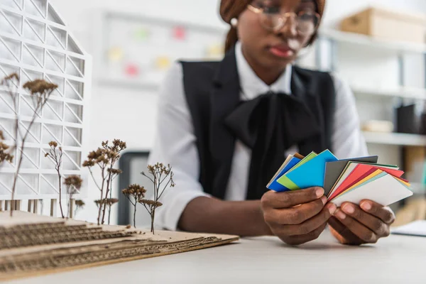 Afro americano donna adulto architetto in bicchieri tenendo campioni di colore e lavorando sul progetto di costruzione in ufficio — Foto stock