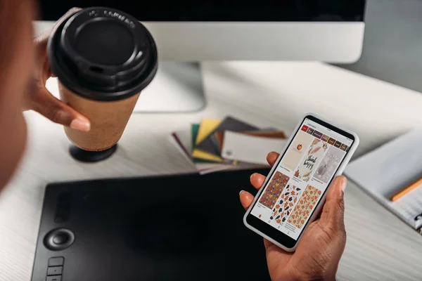 Vista cortada de Africano americano mulher adulta empresária segurando café para ir e smartphone com aplicativo pinterest na tela — Fotografia de Stock