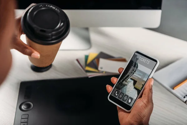 Vista ritagliata di afroamericana donna d'affari in possesso di caffè per andare e smartphone con i biglietti online app sullo schermo — Foto stock
