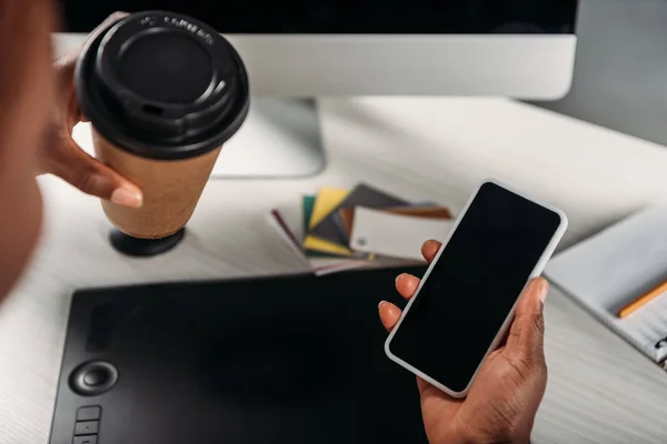 Vista cortada de mulher empresária afro-americana segurando café para ir e smartphone com tela em branco — Fotografia de Stock