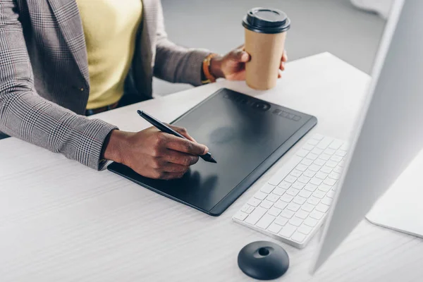 Visão parcial do designer afro-americano segurando café para ir e usando tablet gráfico no local de trabalho — Fotografia de Stock