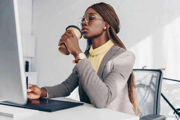 Красива впевнена афроамериканська бізнес-леді, використовуючи графічний планшет і пити каву, щоб піти на робочому місці — стокове фото