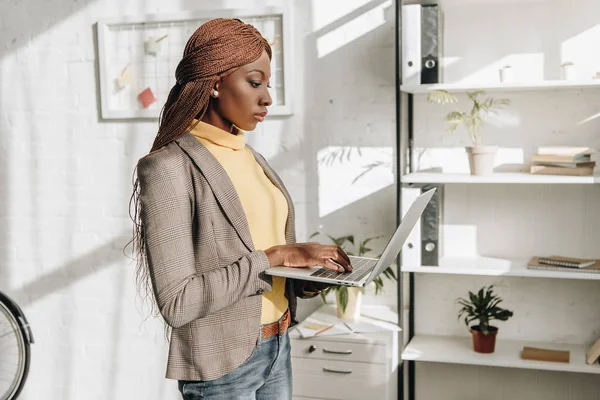 Взгляд сбоку на серьезную африканскую предпринимательницу, держащую ноутбук на рабочем месте — стоковое фото