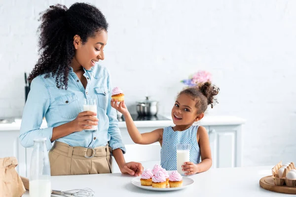 Happy african american daughter showing cupcake to mother in kitchen — Stock Photo