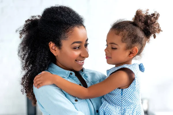 Lächelnd afrikanisch-amerikanische Mutter und Tochter, die sich in der Küche umarmen und einander anschauen — Stockfoto