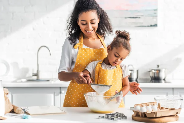 Sonriente afroamericana madre e hija preparando masa y tamizar harina en la cocina — Stock Photo
