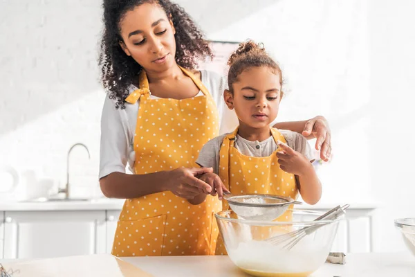 Madre e figlia afroamericana che preparano l'impasto e setacciano la farina insieme in cucina — Foto stock