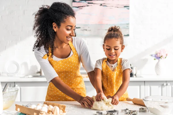 Cheerful african american mother and daughter kneading dough in kitchen — Stock Photo