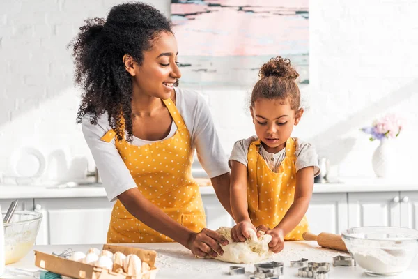 Attractive african american mother and adorable daughter kneading dough in kitchen — Stock Photo