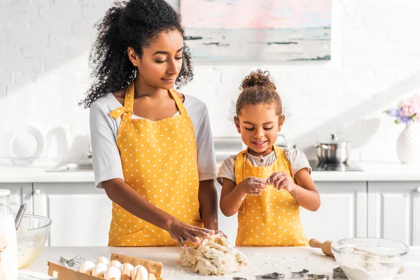 Madre e hija afroamericana preparando postre y amasando masa en la cocina - foto de stock