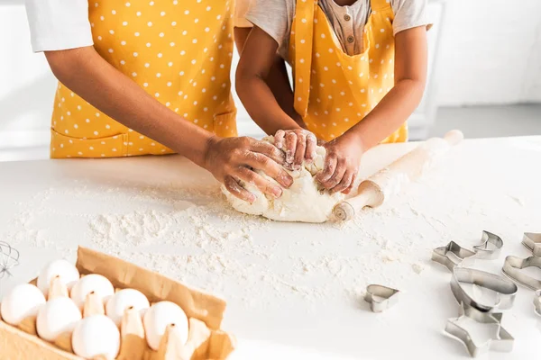 Image recadrée de la mère afro-américaine et sa fille pétrissant la pâte dans la cuisine — Photo de stock