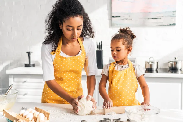 African american mother and daughter kneading dough together on table in kitchen — Stock Photo