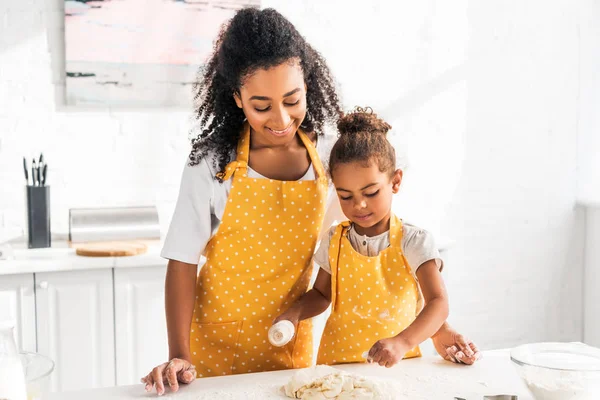 Afro-américaine mère et fille rouler la pâte avec rouleau à pâtisserie dans la cuisine — Photo de stock