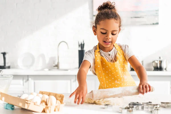 Adorable african american child rolling dough with rolling pin in kitchen — Stock Photo
