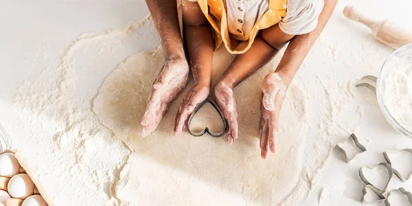 Zugeschnittenes Bild einer afrikanisch-amerikanischen Mutter und Tochter bei der Zubereitung von Keksen mit herzförmiger Form in der Küche — Stockfoto