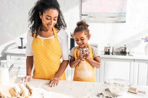 Glücklich afrikanisch-amerikanische Mutter und Tochter suchen Teig für Plätzchen in der Küche — Stockfoto