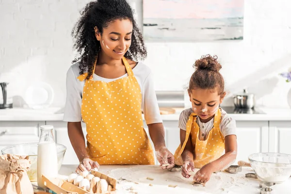 Madre e hija afroamericana preparando galletas con moldes en casa - foto de stock