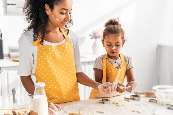Madre e hija afroamericanas seguras de sí mismas preparando galletas con moldes en la cocina - foto de stock
