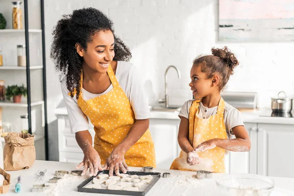 Sonrientes afroamericanos madre e hija preparando galletas y mirándose en la cocina - foto de stock