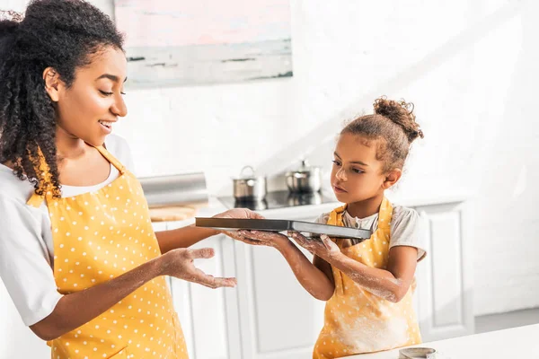 Afro-americana mãe e filha segurando bandeja com biscoitos não cozidos na cozinha — Fotografia de Stock