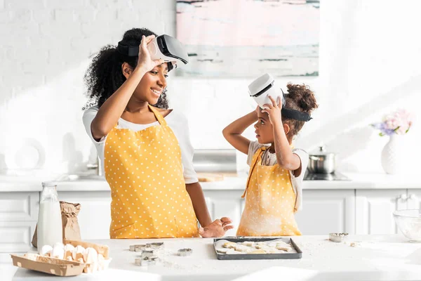 Африканская американская мать и дочь готовят тесто в гарнитурах виртуальной реальности и смотрят друг на друга на кухне — стоковое фото