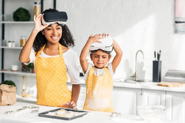 African american mother and daughter preparing dough and wearing virtual reality headsets in kitchen — Stock Photo