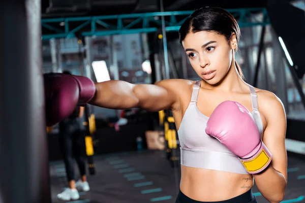 Atractiva chica boxeadora en guantes de boxeo lanzando golpes en el gimnasio - foto de stock