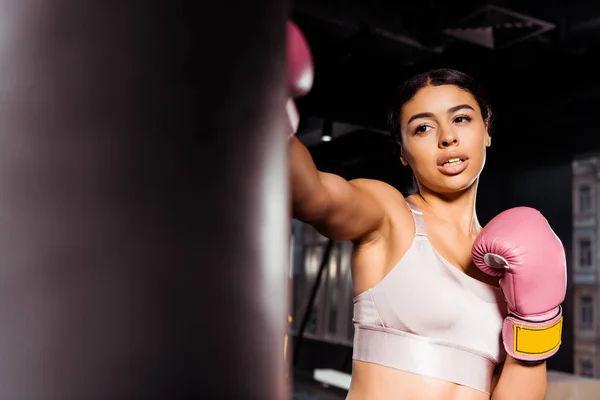 Atractiva chica fuerte en guantes de boxeo rosa practicando boxeo en el gimnasio - foto de stock