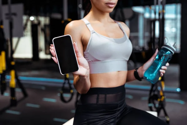 Vista parcial de la mujer deportiva sosteniendo teléfono inteligente en el gimnasio - foto de stock