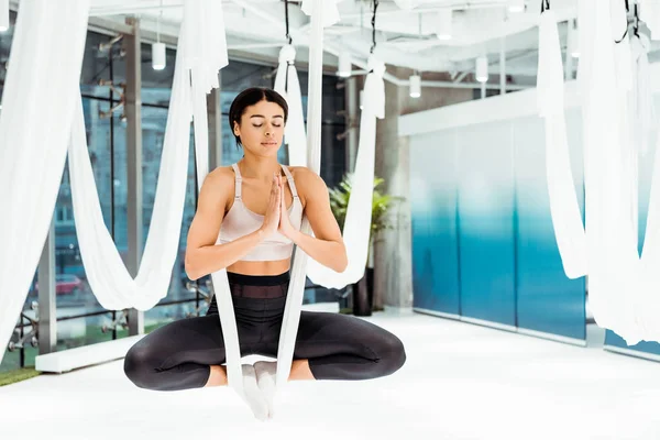 Ragazza rilassata che pratica yoga antigravità in posizione di loto con gesto namaste mudra in studio — Foto stock