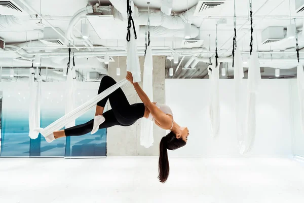 Привлекательная девушка практикует антигравитационную йогу в инверсной позиции в студии — стоковое фото