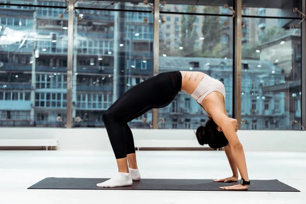 Fille sportive faisant des exercices d'étirement dans la pose de pont sur le tapis dans la salle de fitness avec des fenêtres panoramiques — Photo de stock