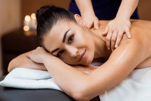 Attractive young woman smiling at camera while having massage in spa salon — Stock Photo