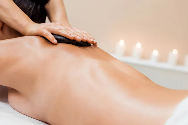 Vista parcial de la mujer joven teniendo masaje de piedra caliente en el salón de spa - foto de stock