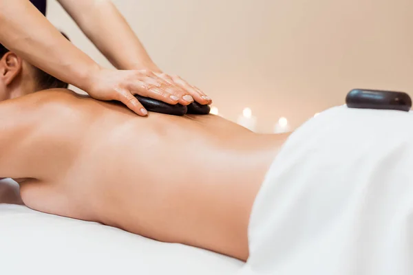 Tiro recortado de mujer joven teniendo masaje de piedra caliente en el salón de spa — Stock Photo