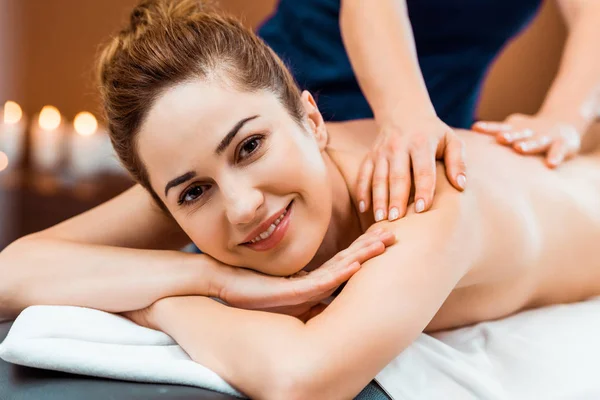 Schöne glückliche junge Frau lächelt in die Kamera, während sie Massage im Wellnessbereich — Stockfoto