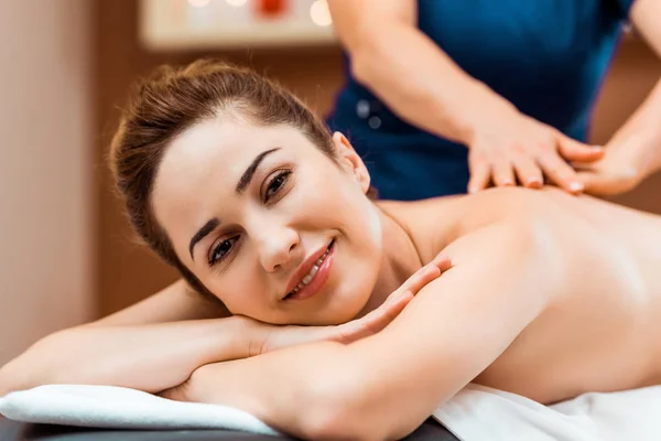 Bela jovem mulher sorrindo para a câmera ao ter massagem no spa — Fotografia de Stock