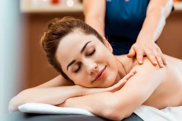 Schöne lächelnde junge Frau mit geschlossenen Augen genießt Massage im Wellnessbereich — Stockfoto