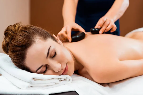 Belle jeune femme aux yeux fermés bénéficiant d'un massage aux pierres chaudes — Photo de stock