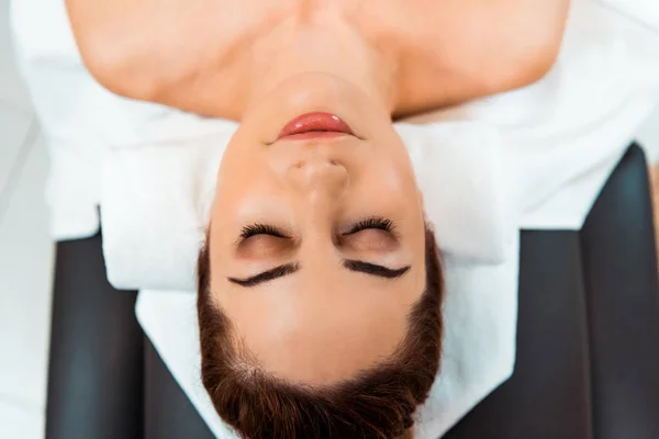Vista superior de la hermosa mujer joven con los ojos cerrados acostado en la mesa de masaje - foto de stock