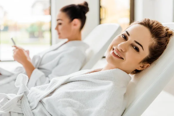 Happy young oman in bathrobe smiling at camera while resting on sunbed in spa — Stock Photo
