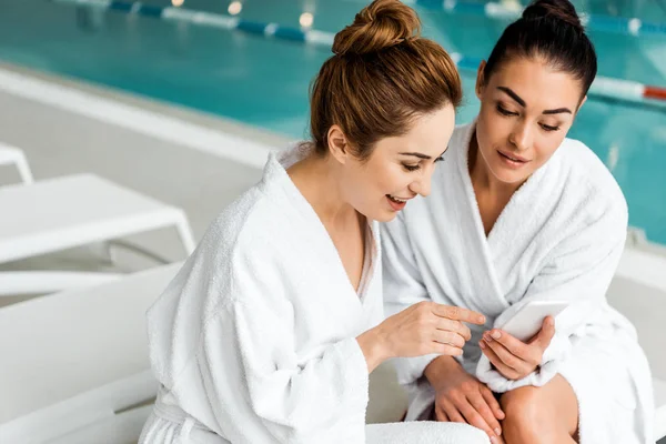 Jeunes femmes heureuses en peignoirs en utilisant un smartphone tout en se reposant dans le spa — Photo de stock