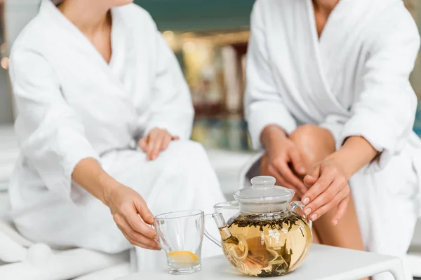 Tiro recortado de las mujeres jóvenes en albornoces beber té de hierbas en el spa - foto de stock
