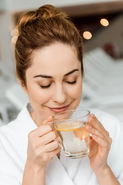 Felice giovane donna in possesso di tazza con bevanda a base di erbe e limone in spa — Foto stock