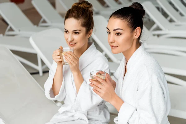 Belas mulheres jovens em roupões de banho segurando xícaras com chá de ervas no spa — Fotografia de Stock