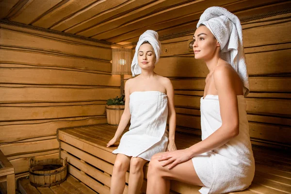 Hermosas mujeres jóvenes relajándose juntas en la sauna - foto de stock