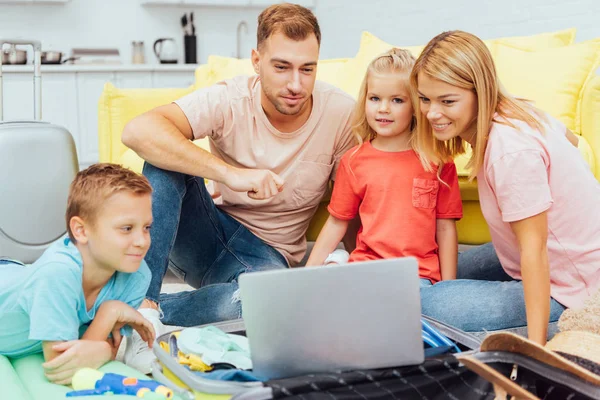 Familia feliz usando el ordenador portátil, planeando vacaciones de verano, embalaje de equipaje y tener un gran tiempo, concepto de viaje - foto de stock