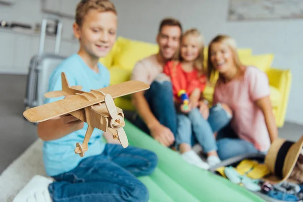 Мальчик играет с игрушкой деревянный самолет с семьей весело на заднем плане и упаковки для летнего отдыха — стоковое фото