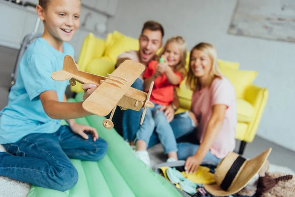 Boy playing with toy wooden airplane with family having fun on background and packing for summer holiday — Stock Photo